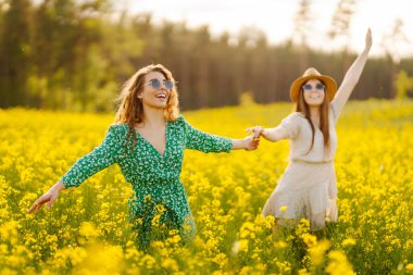 Çiçek açan alanda iki güzel kadın. Moda, tarz kavramı. Aroma ilkbahar doğası sarı çiçek tarlası.