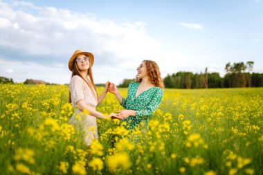 Çiçek açan alanda iki güzel kadın. Moda, tarz kavramı. Aroma ilkbahar doğası sarı çiçek tarlası.