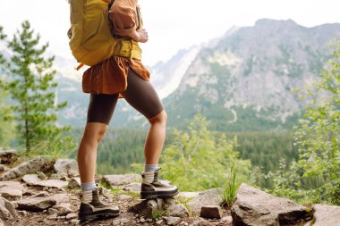 Yürüyüş parkurunda, açık bir dağın tepesinde, yürüyüş botlarıyla kadın bacaklarının yakın çekimi. Seyahat, tatil konsepti.
