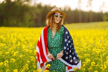 Amerikan bayrağı taşıyan kadın vatansever sahada günbatımının tadını çıkarıyor. 4 Temmuz. Bağımsızlık Günü. 