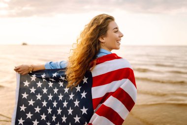 Gün batımında kumsalda Amerikan bayrağı taşıyan kadın vatansever. ABD 4 Temmuz 'u kutluyor. Bağımsızlık Günü kavramı