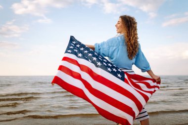 Gün batımında kumsalda Amerikan bayrağı taşıyan kadın vatansever. ABD 4 Temmuz 'u kutluyor. Bağımsızlık Günü kavramı