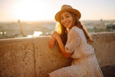 Gün batımında şehrin panoramik manzarasına bakan kadın turistin portresi. Yaşam tarzı, seyahat, turizm, doğa, aktif yaşam.