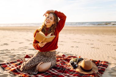 Deniz kenarında piknik yaparken battaniyeye uzanmış kitap okuyan genç bir kadın. Rahatlama, keyif, doğayla baş başa kalma kavramı..