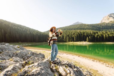 Telefonunu dağda video görüşmesi için kullanan bir kadın. Selfie zamanı. Doğanın tadını çıkarmak ve akıllı telefondan fotoğraf çekmek. Yaşam tarzı, macera, doğa..