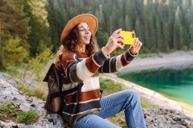 Telefonunu dağda video görüşmesi için kullanan bir kadın. Selfie zamanı. Doğanın tadını çıkarmak ve akıllı telefondan fotoğraf çekmek. Yaşam tarzı, macera, doğa..