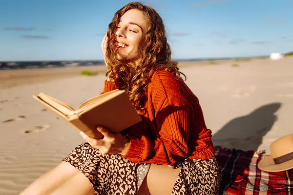 海の近くのビーチでピクニック中に毛布の上に横たわっている間に本を読んでいる若い女性 リラックス 楽しみ 自然との孤独の概念 ストック写真