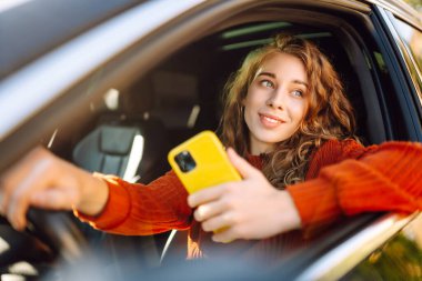 Genç bir kadın telefonu olan bir araba kullanıyor. Boş zaman, seyahat, teknoloji, navigasyon.