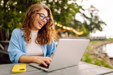 Parktaki bir masada dizüstü bilgisayar kullanarak oturan güzel bir kadın. Eğitim, iş, blog veya serbest çalışma kavramı.