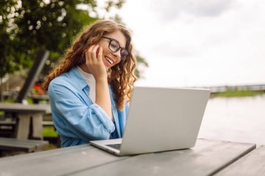Parktaki bir masada dizüstü bilgisayar kullanarak oturan güzel bir kadın. Eğitim, iş, blog veya serbest çalışma kavramı.