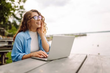 Parktaki bir masada dizüstü bilgisayar kullanarak oturan güzel bir kadın. Eğitim, iş, blog veya serbest çalışma kavramı.