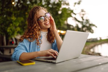 Parktaki bir masada dizüstü bilgisayar kullanarak oturan güzel bir kadın. Eğitim, iş, blog veya serbest çalışma kavramı.