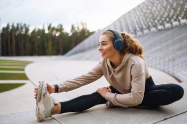 Spor egzersizleri yapan, kulaklıklı, açık havada müzik dinleyen genç ve güzel bir spor sporcusu. Spor, aktif yaşam, spor eğitimi, sağlıklı yaşam tarzı.