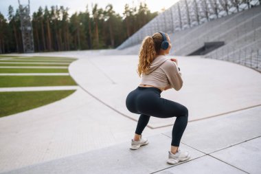 Spor egzersizleri yapan, kulaklıklı, açık havada müzik dinleyen genç ve güzel bir spor sporcusu. Spor, aktif yaşam, spor eğitimi, sağlıklı yaşam tarzı.