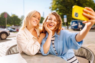 Güzel bayan arkadaşlar açık kahve dükkanında otururken birlikte akıllı telefon selfie 'si çekiyorlar. Moda, güzellik, blog, turizm.