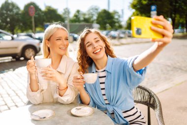 Güzel bayan arkadaşlar açık kahve dükkanında otururken birlikte akıllı telefon selfie 'si çekiyorlar. Moda, güzellik, blog, turizm.