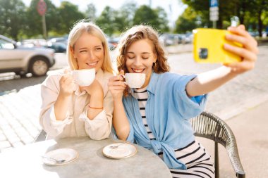 Güzel bayan arkadaşlar açık kahve dükkanında otururken birlikte akıllı telefon selfie 'si çekiyorlar. Moda, güzellik, blog, turizm.