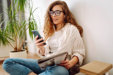 Evde cep telefonu kullanan gülümseyen bir kadın. Bloglama, serbest çalışma, çevrimiçi kurs, uzaktan çalışma, internet konsepti.