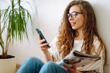 Evde cep telefonu kullanan gülümseyen bir kadın. Bloglama, serbest çalışma, çevrimiçi kurs, uzaktan çalışma, internet konsepti.