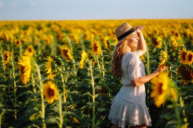 Ayçiçeği tarlasında poz veren güzel bir kadın. Moda, doğa, seyahat ve tatil konsepti.