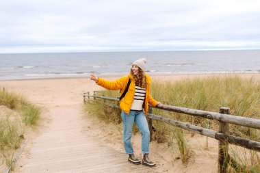 Sarı ceketli mutlu kadın deniz kıyısında yürüyor. Seyahat, turizm konsepti. Etkin yaşam biçimi.