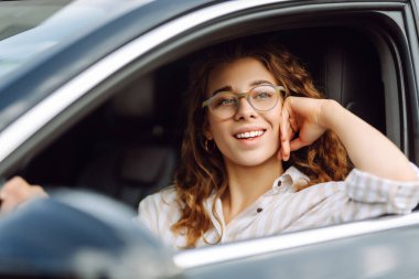 Şehrin etrafında araba süren gülümseyen genç bir kadın. Araba yolculuğu, yaşam tarzı, taşıma konsepti..