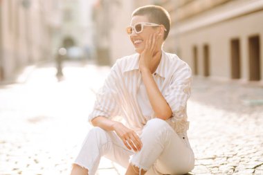 Sokak merdivenlerinde oturan kısa saçlı genç bir kadının portresi. Yaşam tarzı, moda, seyahat kavramı.