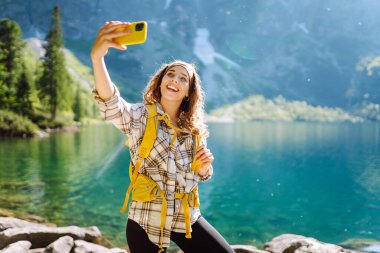 Gülümseyen mutlu kadın akıllı telefonunu kullanarak yürüyüş ve uçuruma tırmanıyor. Yaşam tarzı, seyahat, turizm, aktif yaşam.