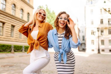 Arka planda poz veren modaya uygun yaz kıyafetleri giymiş iki genç kadın. Yaz eğlencesi konsepti. Yaşam tarzı, moda, seyahat kavramı.