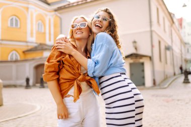 Arka planda poz veren modaya uygun yaz kıyafetleri giymiş iki genç kadın. Yaz eğlencesi konsepti. Yaşam tarzı, moda, seyahat kavramı.