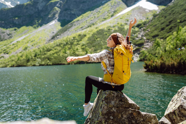 Happy tourist woman  enjoys the view of the mountain lake in sunny weather. Scenery of the majestic mountains. Active lifestyle.