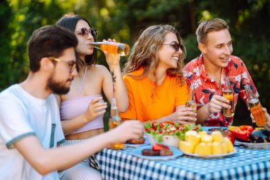 Bir grup arkadaş bira fabrikasının bahçesinde bira bardaklarını tokuşturuyor. Tatil, piknik, hafta sonu, doğa.