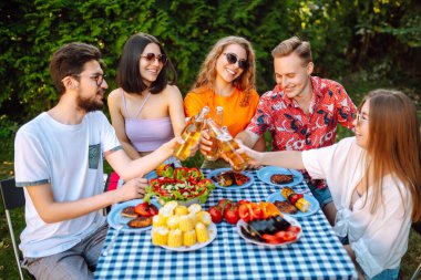 Bir grup arkadaş bira fabrikasının bahçesinde bira bardaklarını tokuşturuyor. Tatil, piknik, hafta sonu, doğa.
