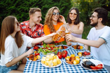 Bir grup arkadaş bira fabrikasının bahçesinde bira bardaklarını tokuşturuyor. Tatil, piknik, hafta sonu, doğa.