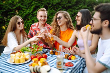 Bir grup arkadaş bira fabrikasının bahçesinde bira bardaklarını tokuşturuyor. Tatil, piknik, hafta sonu, doğa.