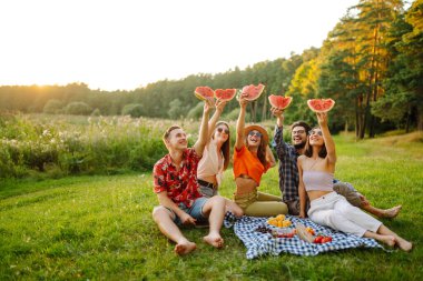 Bir grup arkadaş piknikte karpuz yerken eğleniyorlar. Gıda, seyahat, doğa ve tatil kavramı