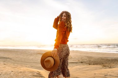 Gün batımında kumsalda yürüyen güzel bir kadın. Seyahat, hafta sonu, rahatlama ve yaşam tarzı konsepti.