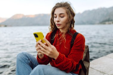 Seddin üzerinde telefonu olan genç bir kadın. Tatillerde turist. Yaşam tarzı, seyahat, doğa, aktif yaşam.