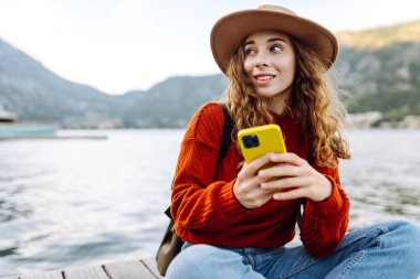 Seddin üzerinde telefonu olan genç bir kadın. Tatillerde turist. Yaşam tarzı, seyahat, doğa, aktif yaşam.