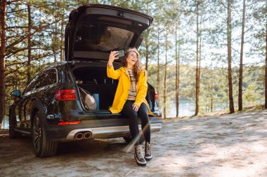 Kadın arabanın bagajında dinleniyor ve selfie çekiyor. Yaşam tarzı, seyahat, turizm, doğa, aktif yaşam.