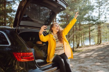 Kadın arabanın bagajında dinleniyor ve selfie çekiyor. Yaşam tarzı, seyahat, turizm, doğa, aktif yaşam.
