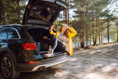 Kadın arabanın bagajında dinleniyor ve selfie çekiyor. Yaşam tarzı, seyahat, turizm, doğa, aktif yaşam.