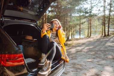 Kadın arabanın bagajında dinleniyor ve selfie çekiyor. Yaşam tarzı, seyahat, turizm, doğa, aktif yaşam.