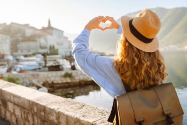 Kalp şeklinde el ele tutuşan bir kadın turist şehrin panoramik manzarasına bakıyor. Yaşam tarzı, seyahat, turizm, aktif yaşam.