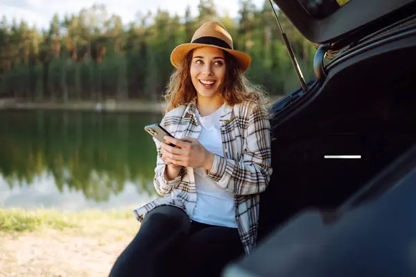 Młoda Kobieta Siedzi Bagażniku Samochodu Używa Smartfona Zewnątrz Koncepcja Podróżowania Zdjęcie Stockowe