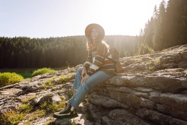 Tepede oturan ve doğanın tadını çıkaran genç bir kadın. Aktif hayat. Yaşam tarzı, seyahat, turizm