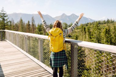 Ağaç tepeleri arasında sırt çantasıyla tahta köprüde genç bir kadın. Özgürlük kavramı, seyahat, yaşam tarzı. 