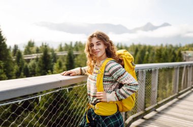 Ağaç tepeleri arasında sırt çantasıyla tahta köprüde genç bir kadın. Özgürlük kavramı, seyahat, yaşam tarzı. 