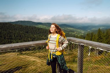 Ağaç tepeleri arasında sırt çantasıyla tahta köprüde genç bir kadın. Özgürlük kavramı, seyahat, yaşam tarzı. 