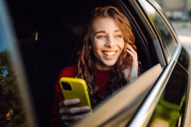 Genç bir kadın arabanın arka koltuğunda oturur ve telefonda konuşur. İş, teknoloji, seyahat, online iletişim kavramı. Taksi..